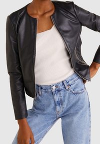 Černá kožená bunda s kulatým výstřihem a předním zipem, stylizovaná s těsným bílým žebrovaným topem a světlomodrými džíny s vysokým pasem.