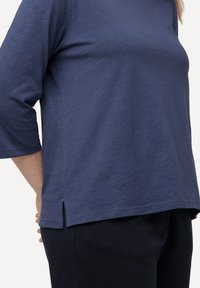 Navy blue, lightweight 3/4 sleeve top featuring a curved hem with side slits. Soft texture, relaxed fit, and minimal stitching detail.