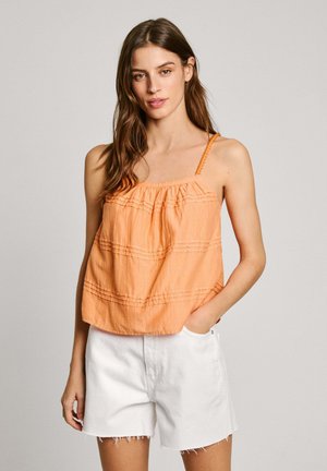 Top arancione senza maniche con dettagli arricciati, spalline intrecciate regolabili e vestibilità morbida, abbinato a pantaloni corti bianchi con strappi. Texture liscia.
