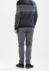 Marinblå och vit mönstrad stickad tröja med ribbade ärmslut, parat med grå strukturerade byxor och svarta skor. Sedd bakifrån.