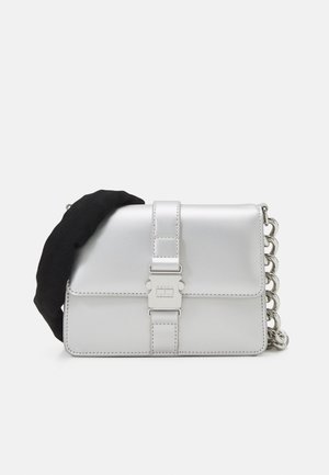 Witte rechthoekige leren crossbodytas met zilveren gespsluiting, brede zwarte stoffen riem aan de linkerkant en stevige zilveren kettingriem aan de rechterkant.