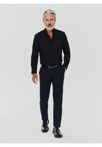 Czarna koszula z długim rękawem zapinana na guziki, zestawiona z granatowymi spodniami i czarnymi błyszczącymi butami. Strój ma dopasowany krój i elegancki design.