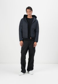 Navy puffer jacket with a hood and zip closure, featuring horizontal quilted pattern. Paired with black cargo pants and white sneakers.