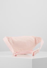 Różowa nerka z tkaniny o zaokrąglonym kształcie, regulowanym pasku i plastikowej klamrze. Gładka tekstura, kompaktowy design, odpowiednia do codziennego użytku.