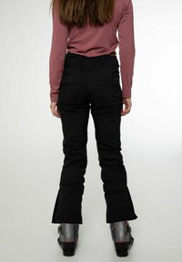 Zwarte skibroek met een slim fit, voorzien van een hoge taille, ritsen bij de enkels en praktische zakken. Gemaakt in combinatie met grijze skiskchoenen.