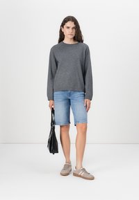 Grå genser, denimshorts, grå joggesko og svart håndveske. Enkelt design, avslappet passform og uformell stil. Flat bakgrunn.