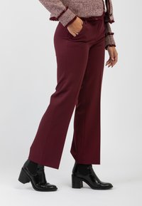 Pantaloni a gamba larga bordeaux con tasche, realizzati in tessuto morbido, abbinati a stivali neri con tacco alla caviglia. Presentano una vestibilità su misura e un design elegante.