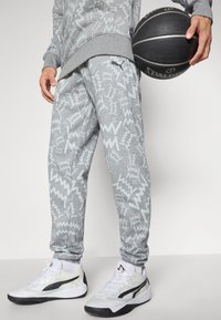 Person i grå mønstrede sweatpants og sneakers, der holder en sort Spalding basketball ved deres side.