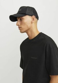 Camiseta de algodón negra con mangas cortas que presenta un sutil logo de "ORIGINALS". Gorra negra con malla en la parte trasera, con visera curvada y detalle del logo en la parte frontal.