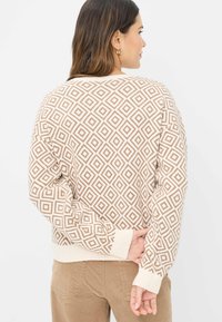 Maglione lavorato a maglia beige con motivo a diamante marrone, polsini e orlo a coste, vestibilità leggermente oversize, tessuto testurizzato. Dettagli del design visibili sul retro.