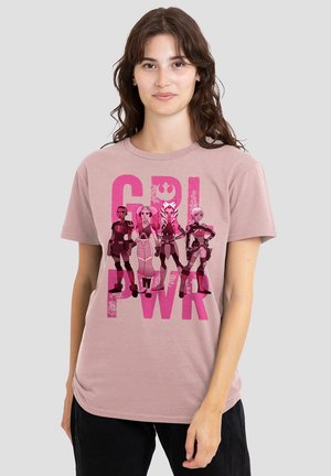 Eine Frau trägt ein pinkes T-Shirt mit vier weiblichen Star Wars-Charakteren, die selbstbewusst über dem in fetten pinken Buchstaben geschriebenen Text "GRL PWR" stehen.