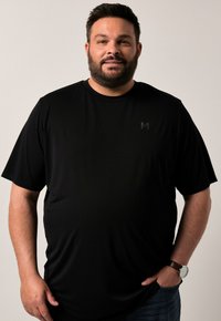 Černé tričko s krátkým rukávem a kulatým výstřihem, vyrobené z hladké, lehké tkaniny. Obsahuje malé logo v tónu na hrudi.