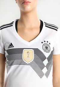 Witte sporttrui met zwarte strepen, V-hals ontwerp, Adidas-logo, FIFA Wereldbeker patch en het embleem van de Duitse Voetbalbond op de borst.