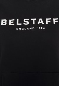 Svart sweatshirt med fet vit text "BELSTAFF" och "ENGLAND 1924" tryckt framtill. Slät textur, rundad halsringning.