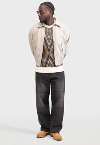 Light beige cropped jacket, patterned brown sweater, black wide-leg pants, and tan clogs. Accessories include gold sunglasses.