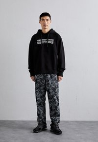 Black hoodie with white "COUTURE" text, paired with black pants featuring a contrasting intricate gray pattern; black sneakers complete the outfit.