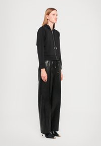 Zwarte cropped hoodie met een rits aan de voorkant, lange mouwen en een trekkoord. Gecombineerd met hooggetailleerde zwarte leren wijde broek en puntige hakken.