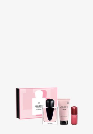 Coffret cadeau Shiseido Ginza avec flacon de parfum, tube de lotion pour le corps parfumée et petit flacon de sérum rouge sur fond pâle.
