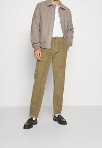 Pantaloni in velluto a coste color corda con gamba dritta, abbinati a un blazer in feltro grigio chiaro e a una t-shirt bianca, completati da mocassini neri.