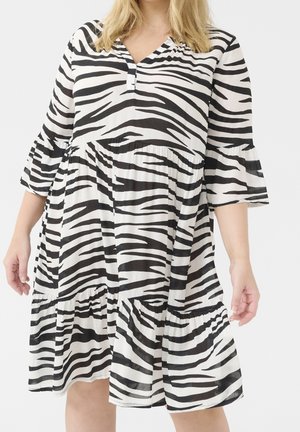 Kobieta ubrana w luźną czarno-białą sukienkę w zebra print z rękawami do łokcia i falbanową spódnicą.