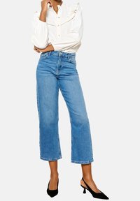 Vit blus med volangdetaljer, ljusblå beskurna jeans och svarta spetsiga klackar. Har standard knappstängning och avslappnad passform.