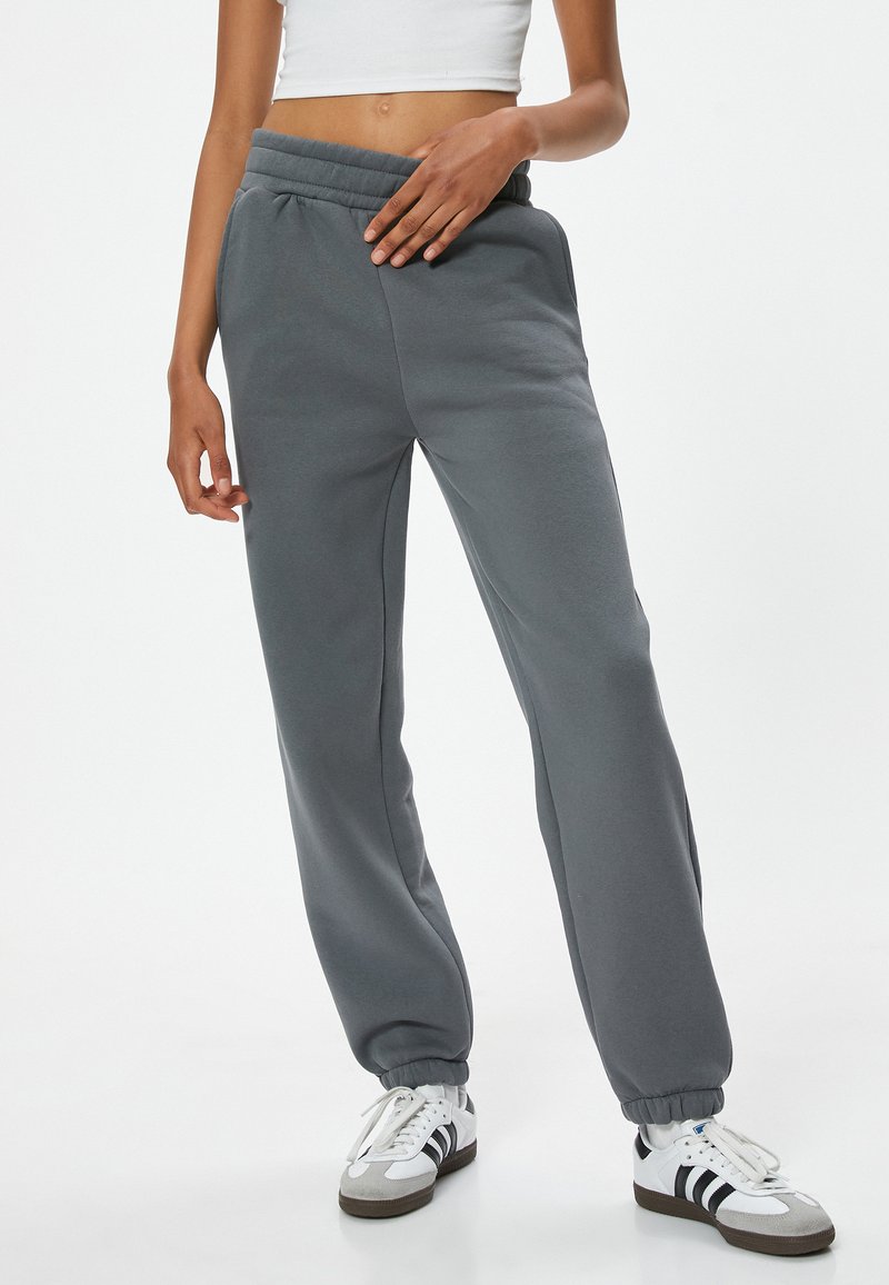Grijze sweatpants van zachte stof, met een relaxte pasvorm, elastische tailleband en boorden, gecombineerd met witte sneakers.