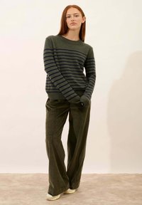 Sweter w oliwkowo-zielone paski z granatowymi poziomymi paskami, zestawiony z szerokimi spodniami z oliwkowego sztruksu. Miękka tekstura, prążkowane mankiety i dół.