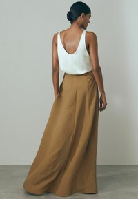 Top de tirantes en forma de V color crema combinado con una larga y fluida falda maxi marrón. La falda presenta una superficie texturizada y un diseño de cintura alta.