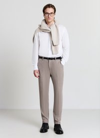 Leichtes weißes Hemd kombiniert mit strukturierten beigen Hosen und schwarzen Lederstiefeln. Ein gestrickter beiger Schal liegt lässig um den Hals.