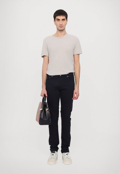 Γκρι κοντομάνικο μπλουζάκι, σκούρο τζιν παντελόνι και λευκά αθλητικά παπούτσια. Κρατάει μια μαύρη τσάντα χειρός με πολύχρωμες ρίγες και χρυσές λεπτομέρειες.