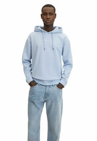 Felpa azzurro chiaro con tasca a marsupio frontale, cappuccio con stringhe e maniche a costina, abbinata a jeans azzurro chiaro, modello in piedi.