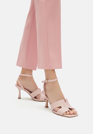 Różowe sandały na wysokim obcasie z otwartym palcem, ozdobione wycięciami, paseczkami wokół kostki oraz teksturowaną powierzchnią. Kwadratowy nosek i smukły obcas.