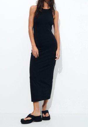 Robe longue noire sans manches avec une coupe ajustée. Associée à des sandales noires à plateforme épaisses. Tissu lisse et extensible avec une finition mate.