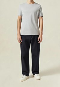 Szary t-shirt z krótkim rękawem i okrągłym dekoltem, zestawiony z ciemnymi dżinsami i białymi trampkami. Strój cechuje się luźnym krojem i prostym designem.