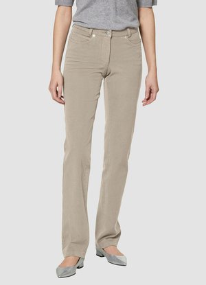 Persoon in beige rechte broek, grijs top met driekwartmouwen en zilveren schoenen met lage hakken, staande tegen een effen achtergrond.