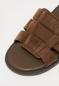 Sandal in suede marrone con ampie cinghie sovrapposte e una soletta in pelle marrone scura liscia, dotata di suola in gomma nera testurizzata.