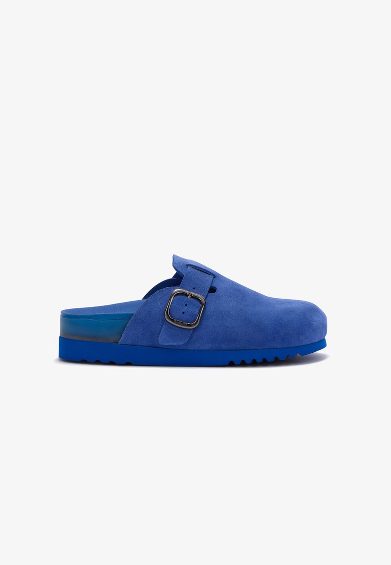 Blue suede slip-on clog with a wide adjustable strap and silver buckle, featuring a textured sole and open back for easy wear.