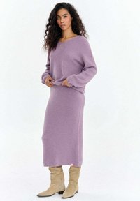 Lawendowy sweter z dzianiny i dopasowana spódnica midi o luźnym kroju i miękkiej teksturze, zestawione z beżowymi, luźnymi kozakami za kolano.