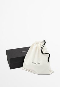 Bawełniana torba na sznurek w kolorze ecru z logo "Massimo Dutti". Czarna prostokątna pudełko z logo z przodu, stanowiąca kontrast dla torby.