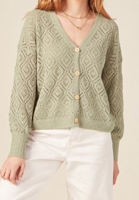 Jasnozielony, dziergany kardigan z motywem diamentów, dekoltem w serek oraz drewnianymi guzikami. Tkanina o fakturze z prążkowaniem na mankietach i dole.