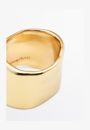Bague en tone or présentant un design lisse et courbé avec une surface polie et une forme légèrement irrégulière. Marquée à l'intérieur avec "Massimo Dutti."