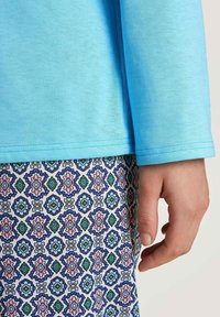  Lichtblauwe blouse met lange mouwen van een textuurstof, gecombineerd met een pantalon met een patroon in een bloemenontwerp in roze, groen en blauw.