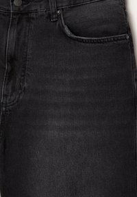 Jeans en denim noir avec un design classique à cinq poches, présentant une légère décoloration, des coutures surpiquées et une fermeture à bouton à la taille.