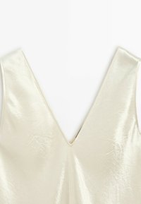 Cream-colored sleeveless top with a deep V-neck and a slightly shiny, textured fabric.