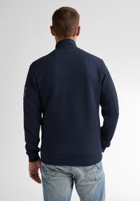 Mörkblå, texturerad sweatshirt med krage och ribbad mudd, med ett diskret vävt mönster och en accentpatch på vänster ärm.