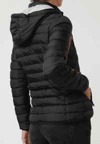 Chaqueta acolchada negra con acabado texturizado, con capucha integrada y detalles en naranja en los laterales, bolsillos con cremallera y puños elásticos.