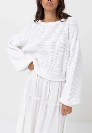 White knitted sweater with a loose fit, wide sleeves, and a ribbed hem, paired with a flowy white tiered dress. Soft texture.