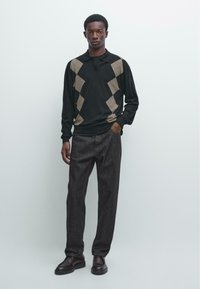 Zwart-bruine gebreide polotrui met diamantpatroon, gecombineerd met donkergrijze broek en bruine lederen schoenen. Eenvoudig, aansluitend ontwerp.