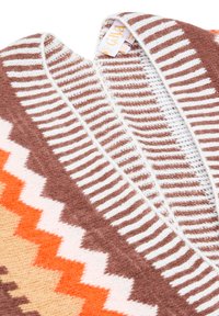 Coperta lavorata a maglia con motivi geometrici in tonalità calde: arancione, marrone e crema. Texture morbida con un design a zigzag. Etichetta visibile.
