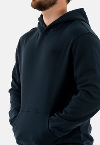 Sudadera azul marino hecha de una tela suave, con un bolsillo tipo canguro, puños acanalados y un logo en relieve en el pecho.
